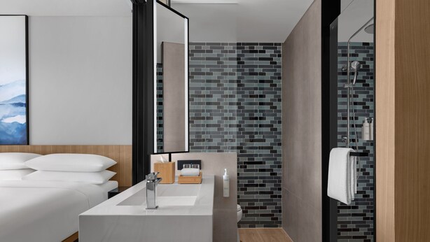 Un baño moderno con un lavabo grande de color blanco, un mueble de tocador de madera y una zona de ducha con pared de azulejos.