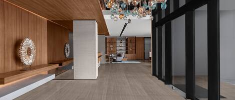 A modern interior with a wooden reception desk, a dining area, and a kitchen in the background.