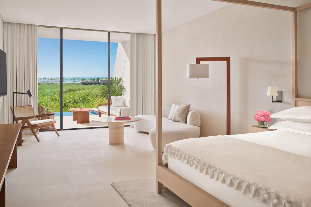 A modern hotel room with a large bed, a flat-screen TV, a sofa, a coffee table, and a view of the ocean.