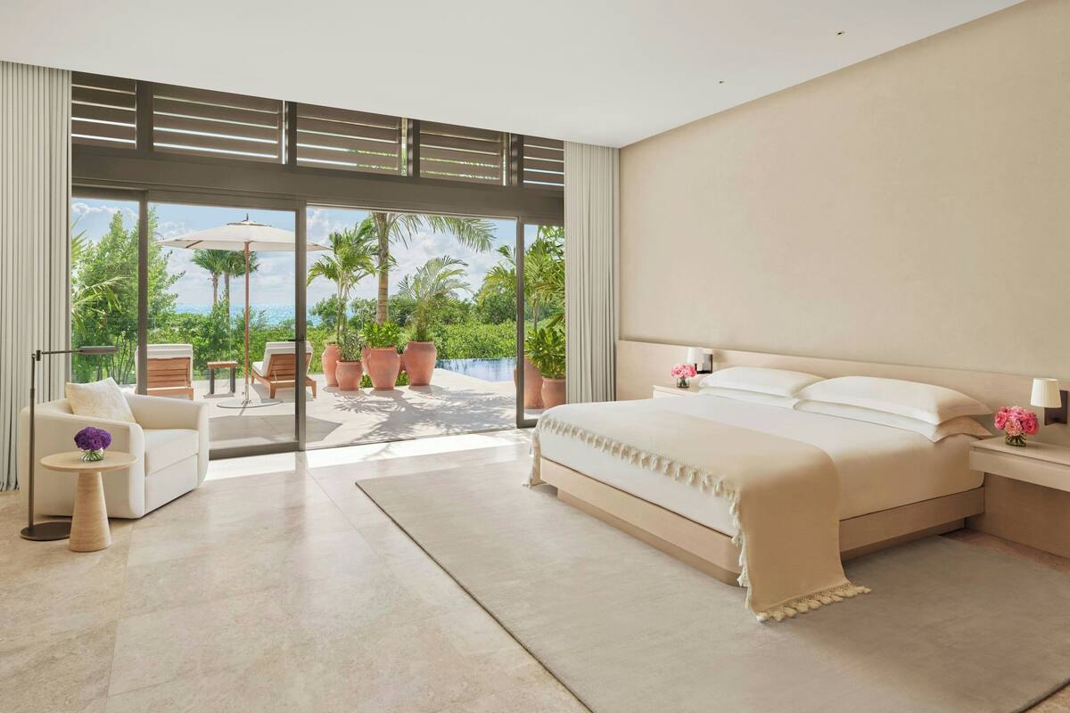 A modern bedroom with a large bed, a sofa, and a dining area with outdoor views.