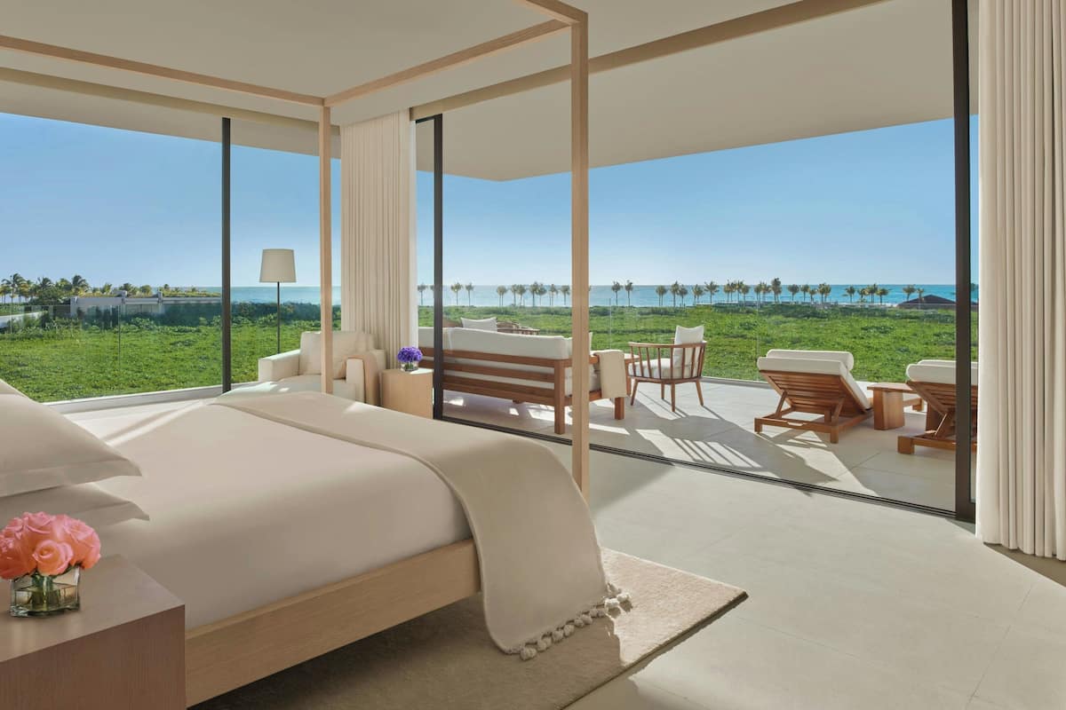 A modern bedroom with a large bed, a view of the ocean, and a balcony with outdoor seating.