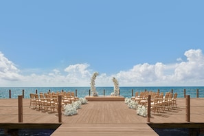 A wooden deck with chairs arranged for an event, overlooking the ocean.
