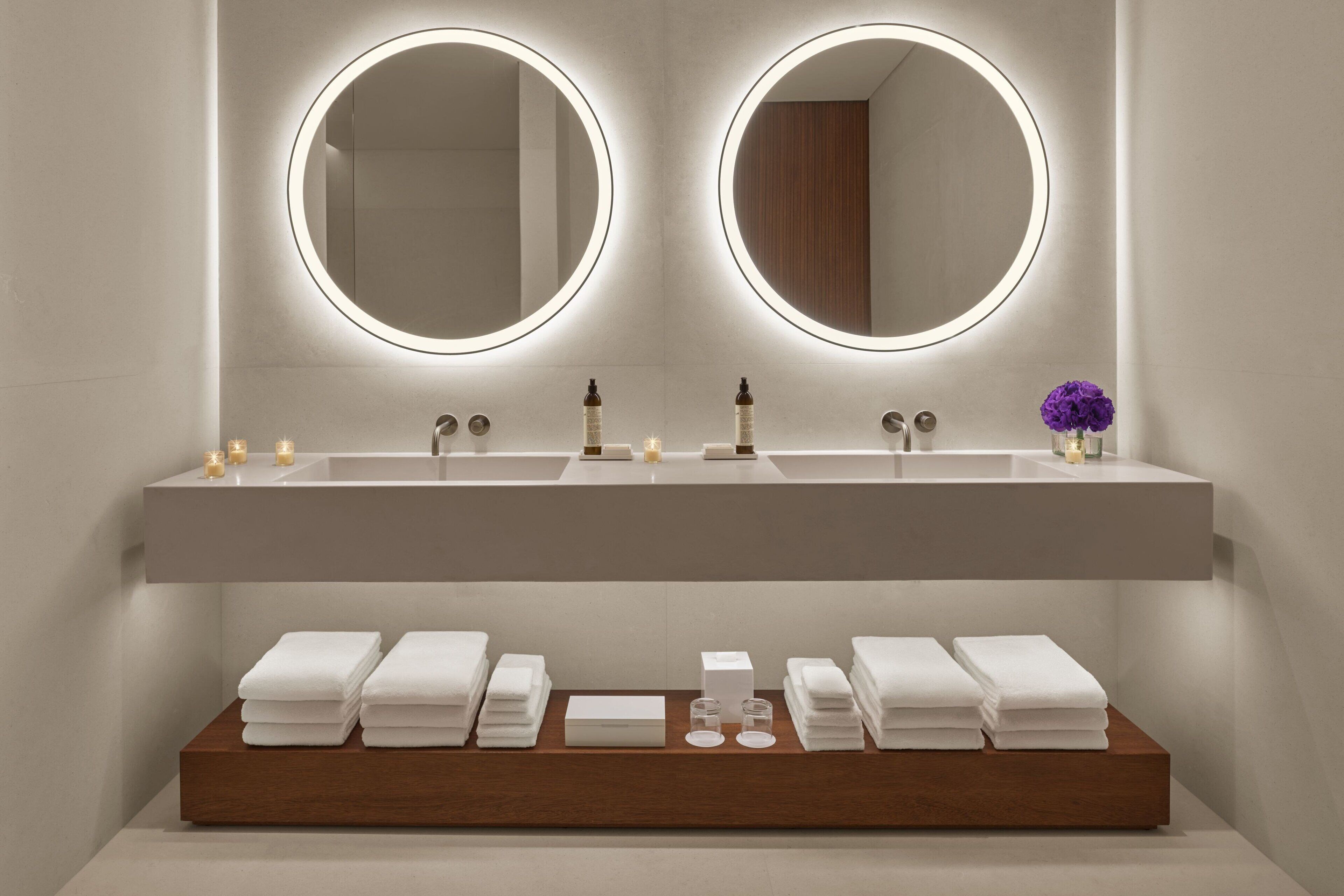 Un baño moderno con dos lavamanos, espejos iluminados y toallas ordenadas.