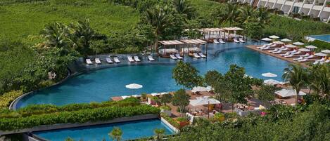 Um resort com uma piscina grande, áreas de descanso e um edifício moderno com varandas.