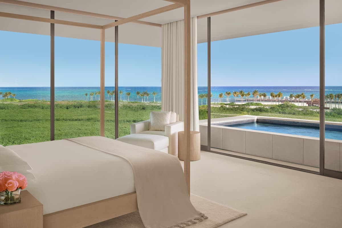 A bedroom with a large bed, a seating area, and a view of the ocean.