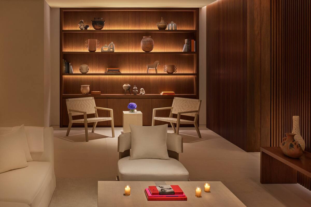 A modern living room with a wooden bookshelf, two armchairs, a small table with books and candles, and a sofa.