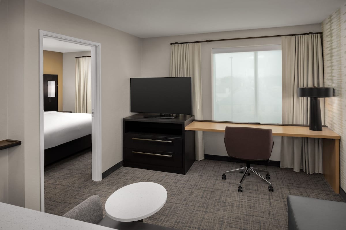 Ein Hotelzimmer mit einem Bett, einem Schreibtisch mit Fernseher, einem Sessel und einem kleinen Tisch.