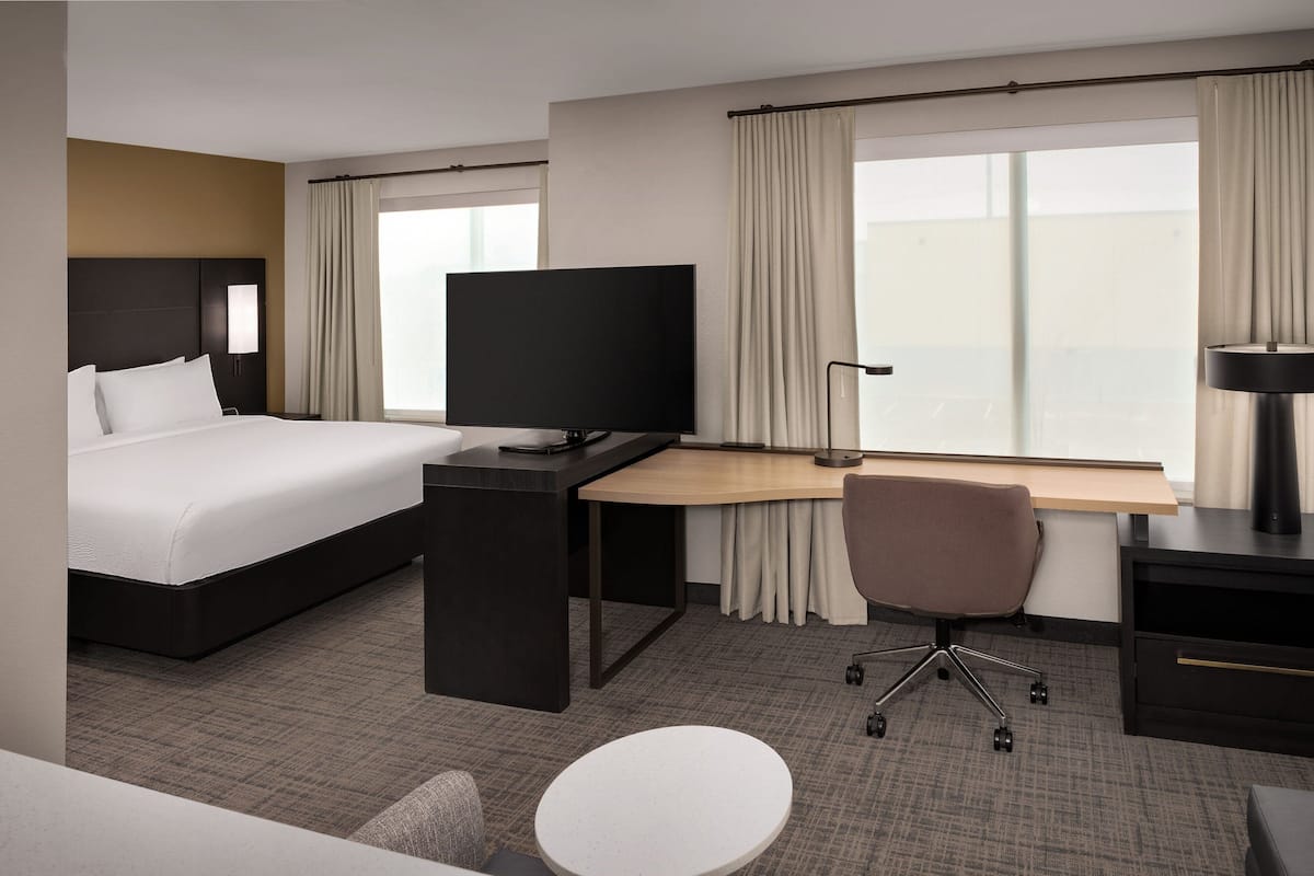 Ein Hotelzimmer mit Bett, Schreibtisch, Stuhl, Fernseher und einem Fenster mit Vorhängen.