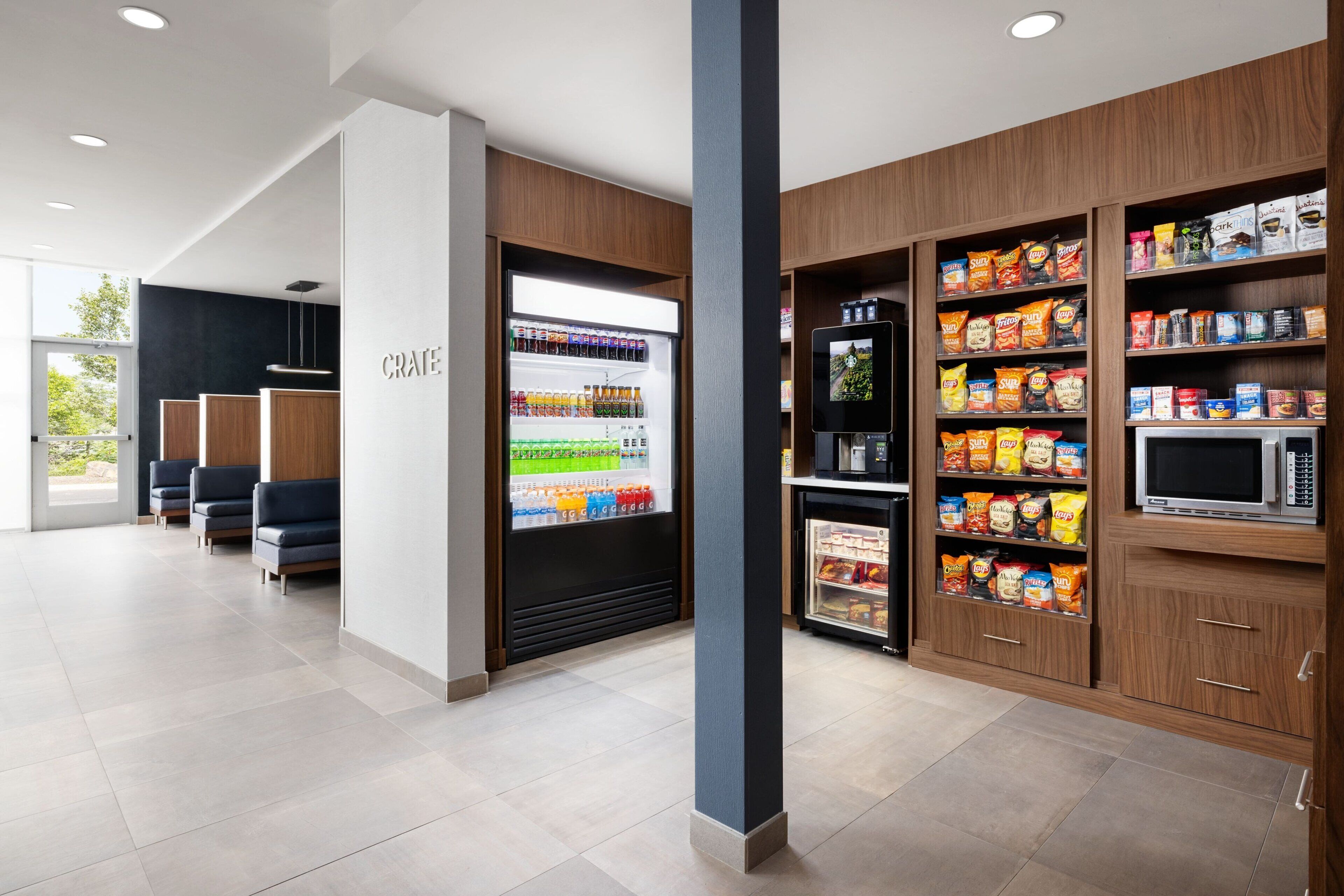 Un moderno vestíbulo de hotel con una zona de estar, una vitrina refrigerada para bebidas y estantes con aperitivos.