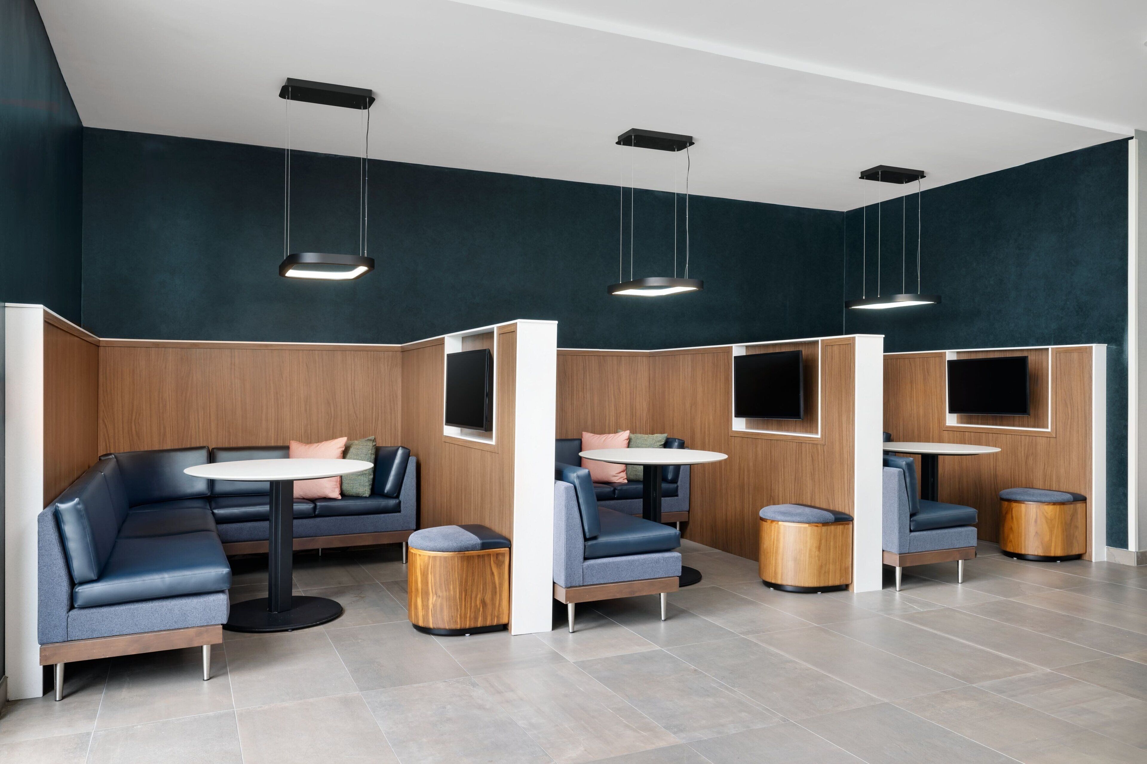 Un espace de détente moderne, aménagé avec différents types de sièges, notamment des canapés et des fauteuils, et doté d’écrans de télévision intégrés.