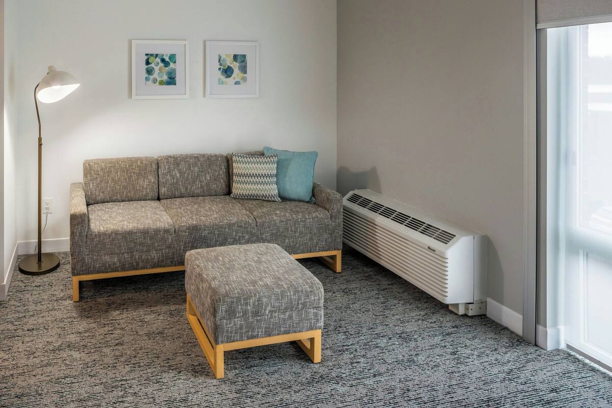 A living room with a grey sofa, a matching ottoman, a floor lamp, and two abstract paintings on the wall.