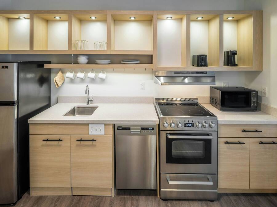 A modern kitchen with stainless steel appliances, wooden cabinets, and built-in lighting.