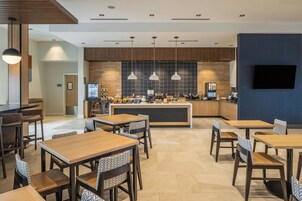 A modern restaurant with wooden tables and chairs, a central bar area, and pendant lighting.