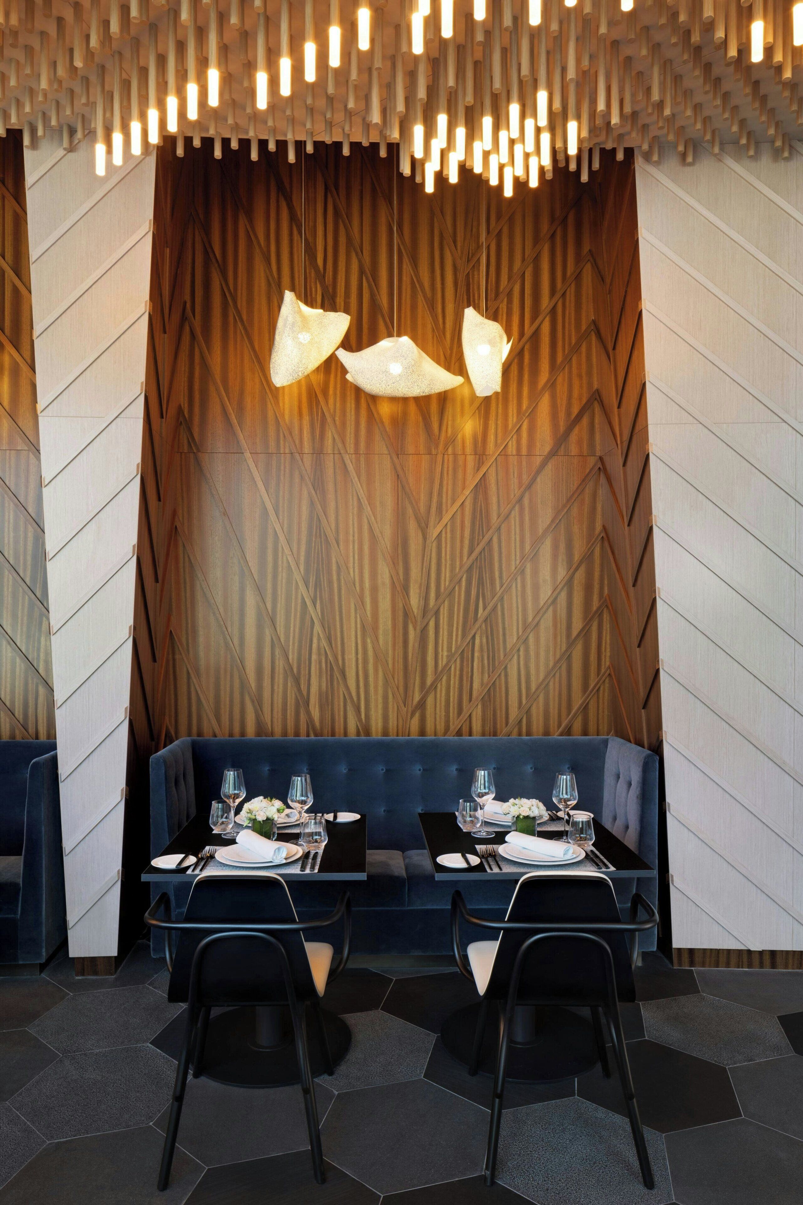 A modern dining area with a wooden wall, a dark blue booth, and a unique ceiling light fixture.