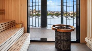 A sauna room with wooden benches, a stone heater, and a large window offering a city view.