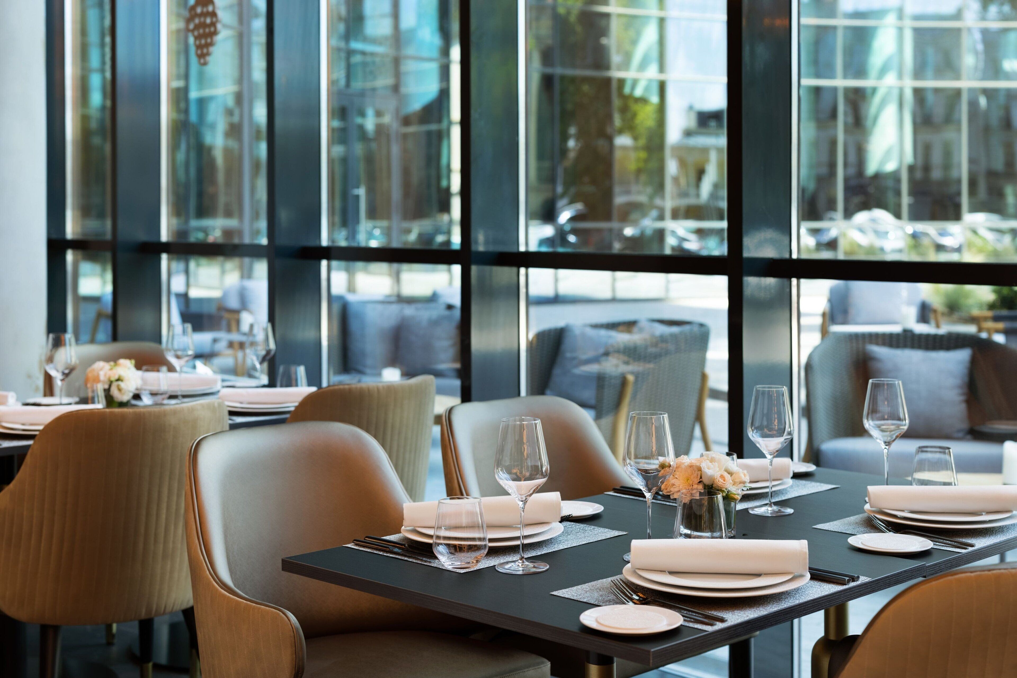 A dining area with tables set for a meal, large windows, and modern chairs.