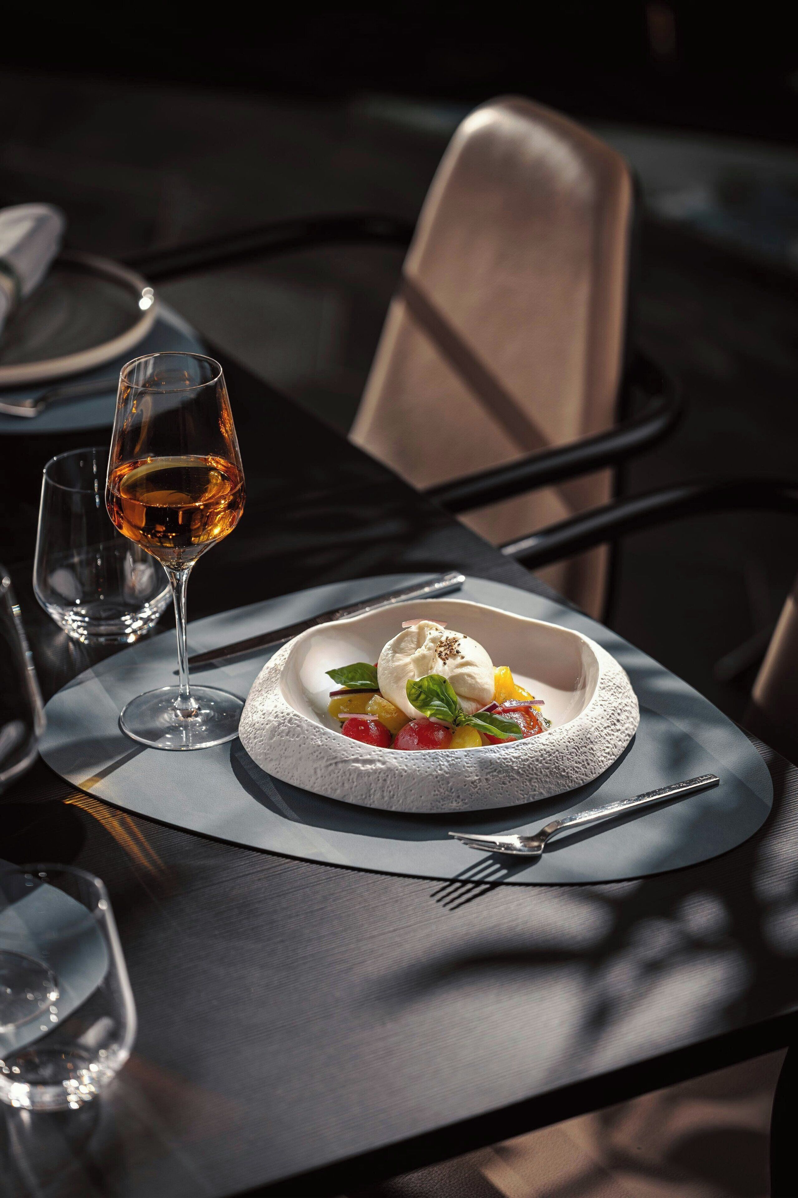 A dining table with a white bowl containing a dessert, a glass of wine, and cutlery.