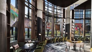 Ein modernes Interieur mit großen Fenstern, grünen und gelben Sesseln und Kunstwerken an den Wänden.