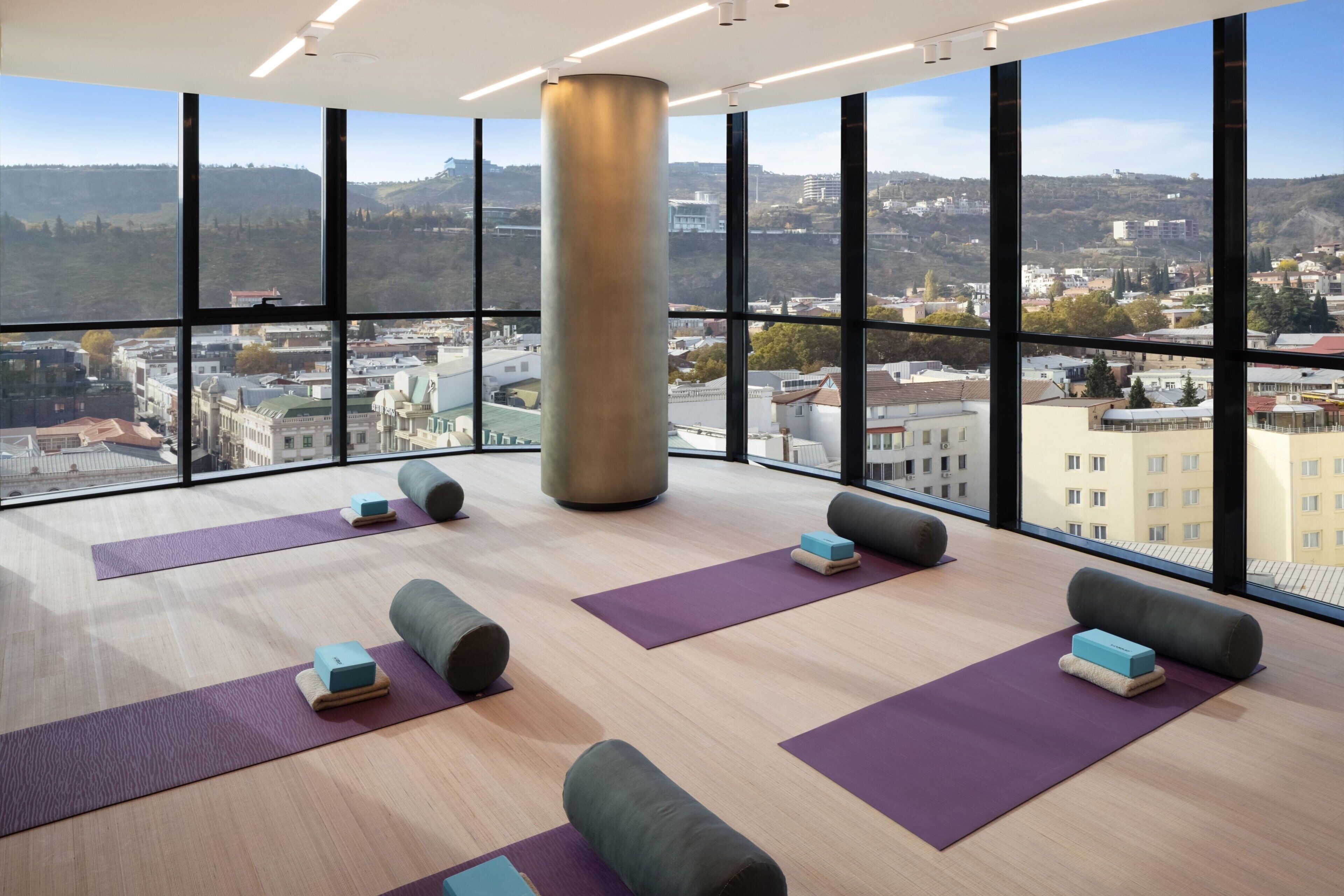 A spacious room with large windows offering a city view, yoga mats, and blocks arranged for exercise.