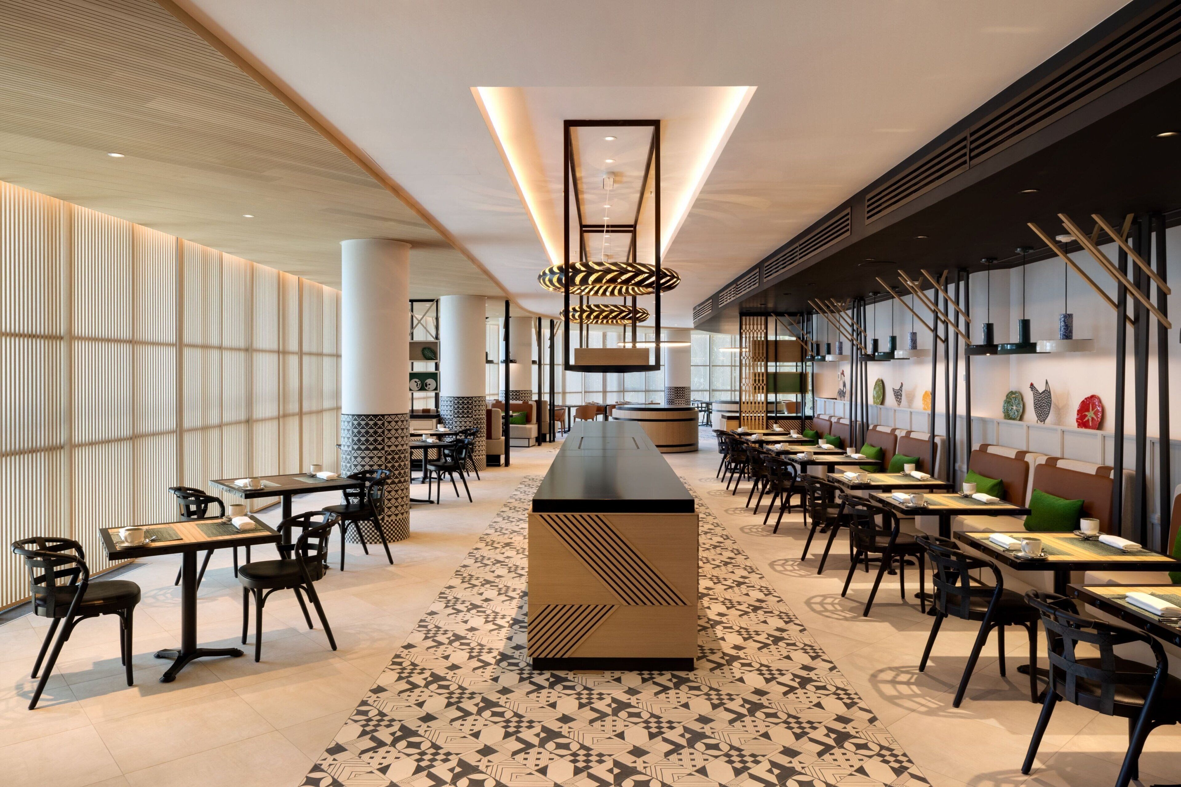 A modern restaurant with a long counter, black chairs, and patterned floor tiles.