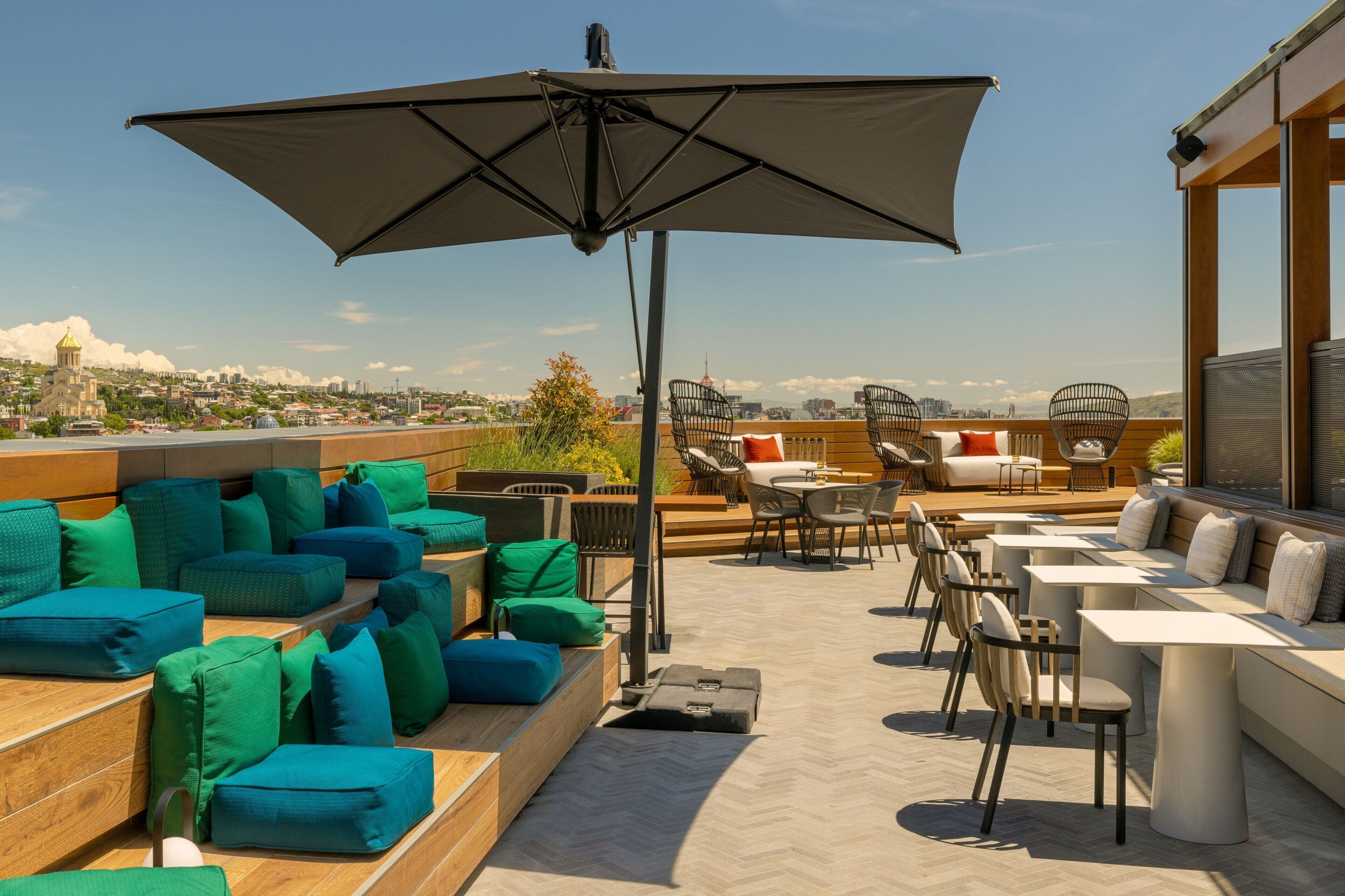 A rooftop terrace with seating areas, tables, and a large umbrella.