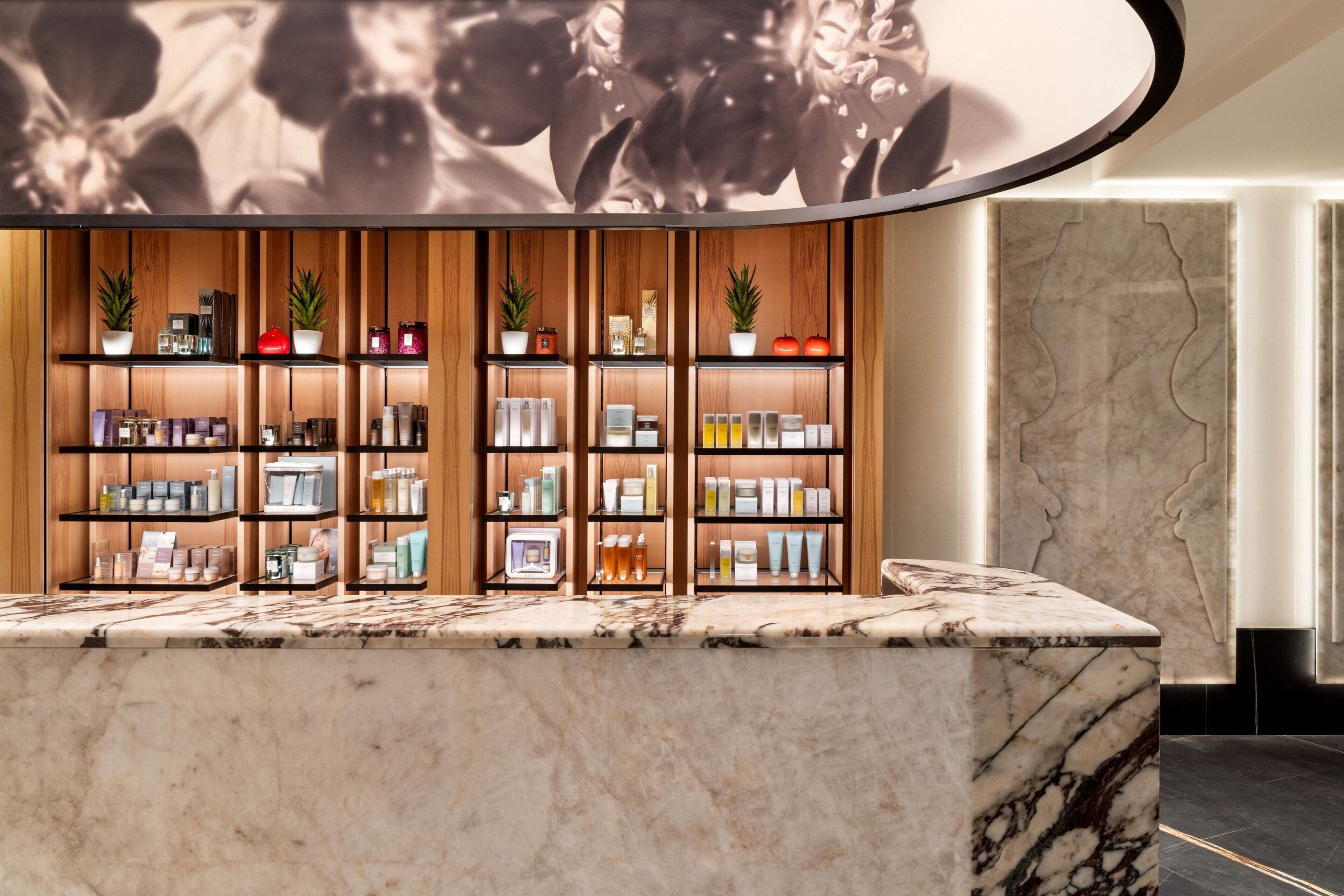 Zona de recepción con mostrador de mármol, estanterías de madera con diversos productos y techo decorativo.