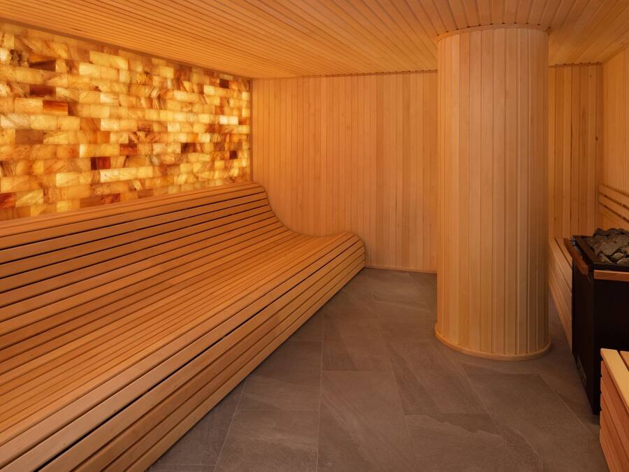 Una sauna con bancos de madera, suelo de baldosas y una pared con diseño texturizado.