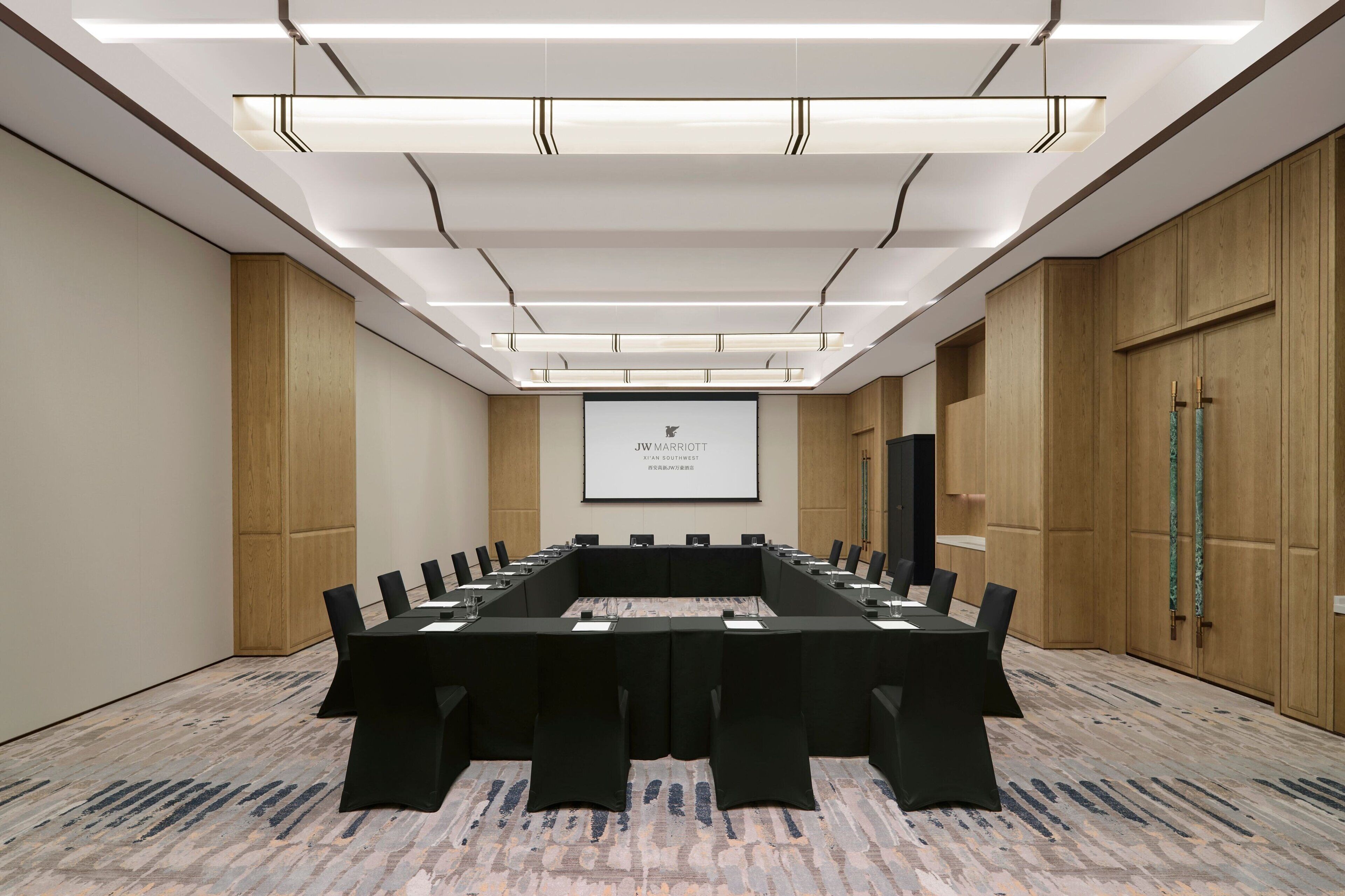 A conference room with a long table, black chairs, and a projector screen displaying text.