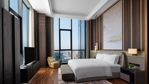 Ein modernes Hotelzimmer mit einem großen Bett, einem Fernseher, einer Couch und Blick auf die Stadt.