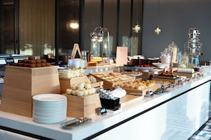 A buffet with various food items and a stack of white plates.