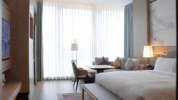 Una habitación de hotel con una cama grande, un escritorio, una silla y una ventana con cortinas translúcidas.
