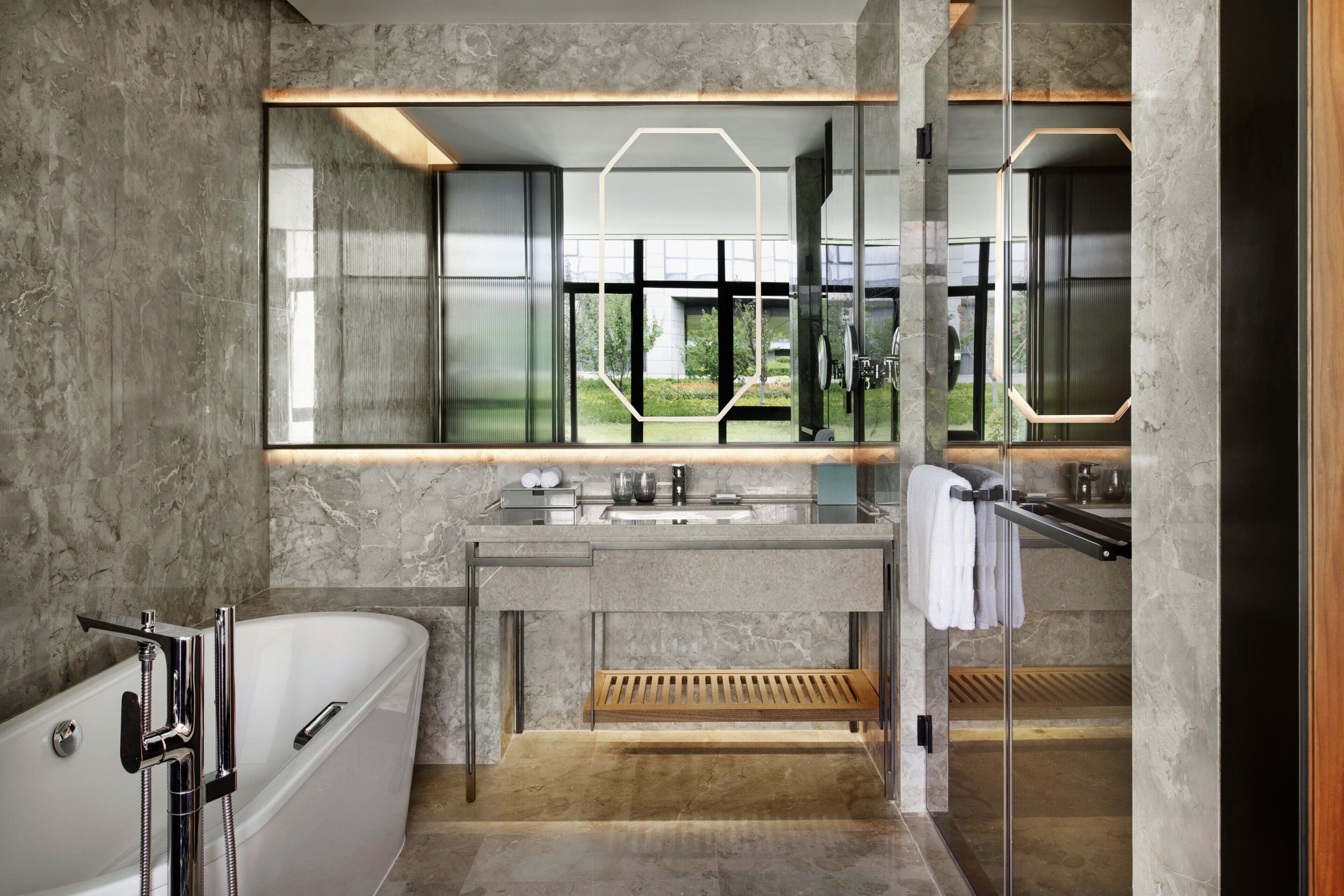 A modern bathroom with a large bathtub, a vanity with a mirror, and a window offering a view of the outdoors.