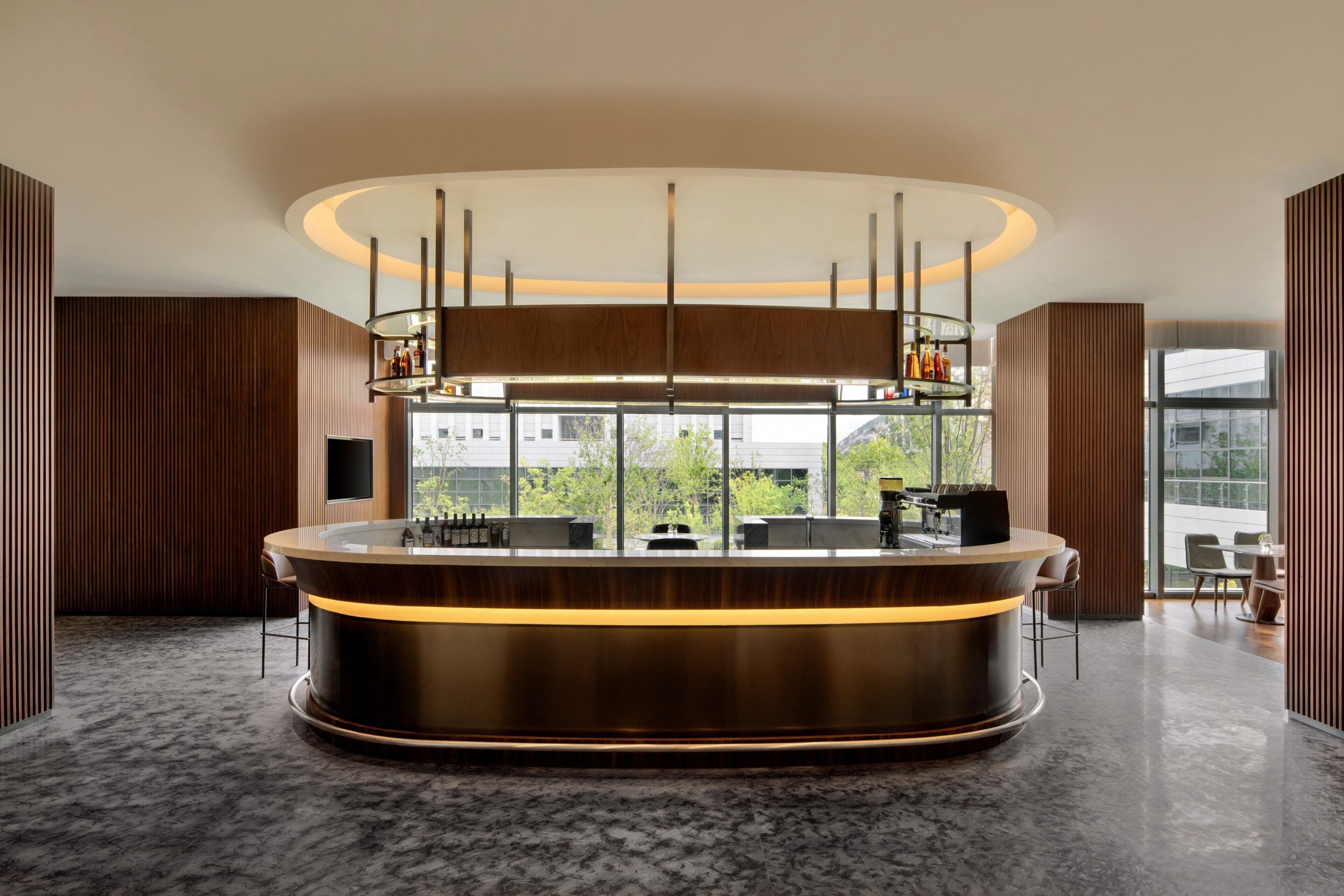 A modern bar area with a curved counter, a glass display case, and a large window offering a view of the outdoors.