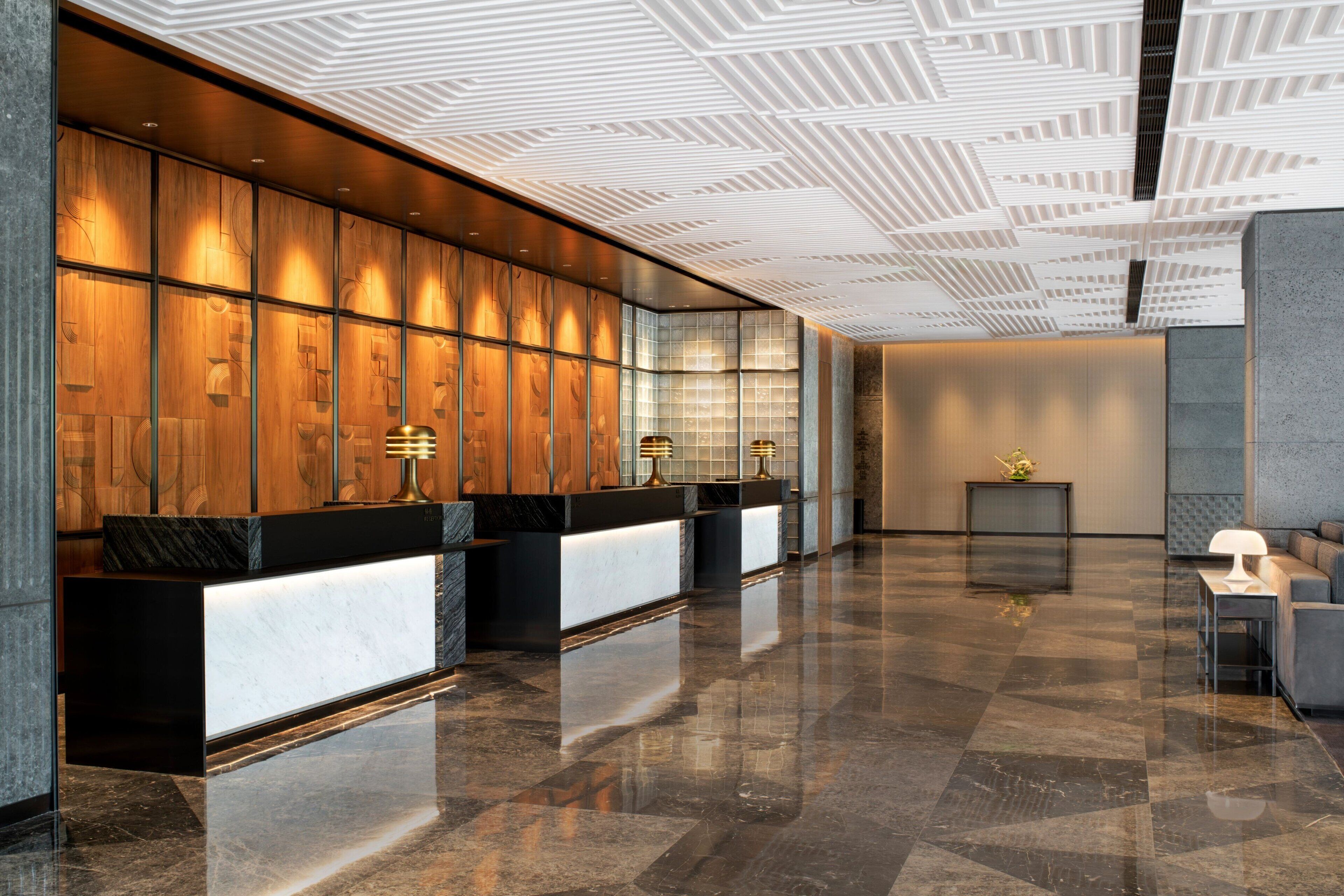 A modern reception area with a wooden panel wall, a black reception desk, and a polished marble floor.