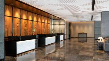 A modern reception area with a wooden panel wall, a black reception desk, and a polished marble floor.