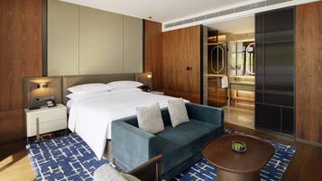 Habitación de hotel moderna con una cama grande, un sofá, una mesita y un baño visible a través de una puerta abierta.