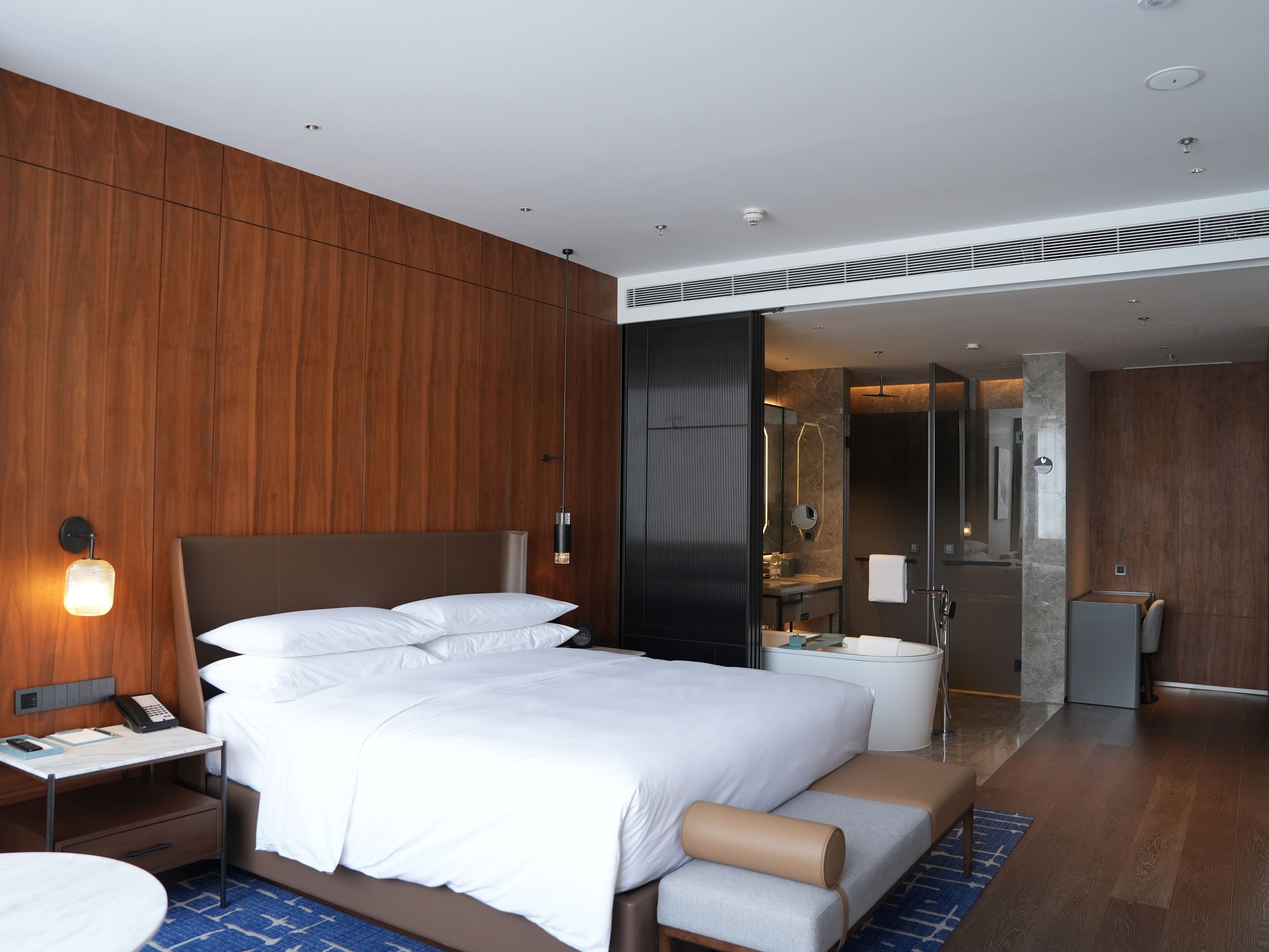 Une chambre d’hôtel moderne, dotée d’un grand lit, de tables de chevet, d’un bureau et d’une salle de bain visible à travers une porte ouverte.