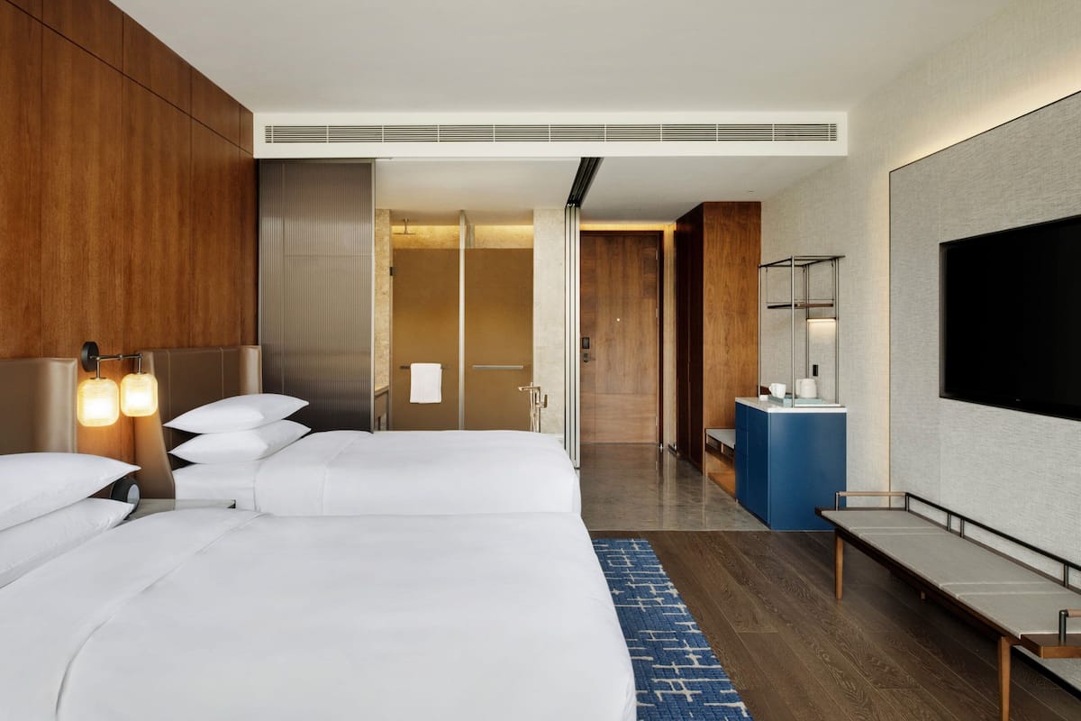 A modern hotel room with a large bed, a bathroom with a mirror, and a TV mounted on the wall.