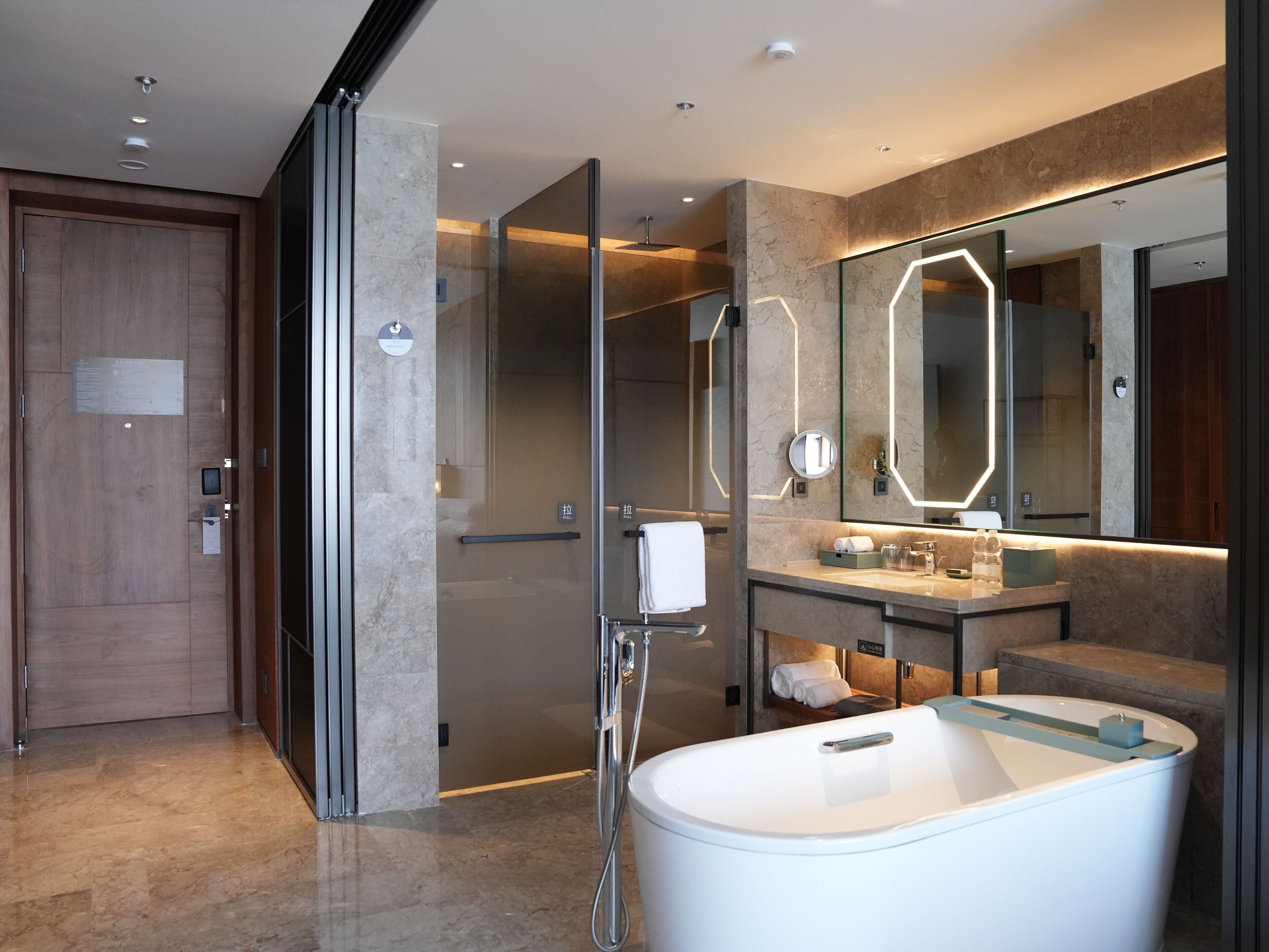 Un baño moderno con una bañera independiente, un espejo grande con iluminación geométrica y una puerta de madera.