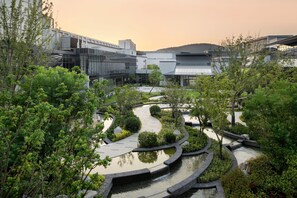 Un moderno complejo de edificios con un jardín ajardinado que incluye una fuente sinuosa y varias especies de árboles.
