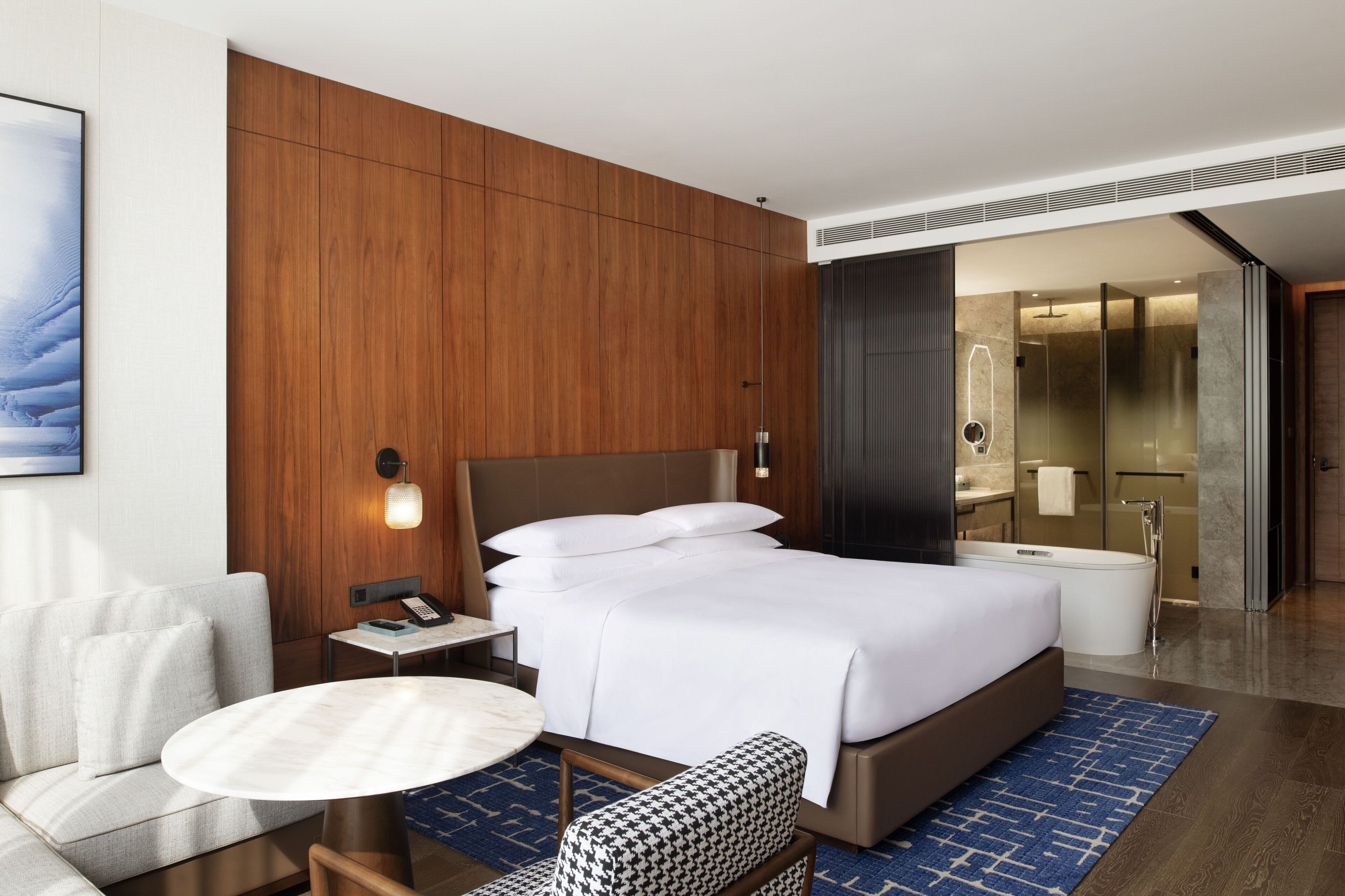 Une chambre d’hôtel moderne dotée d’un grand lit, d’une table de chevet, d’une chaise, d’une table ronde et d’une salle de bain avec baignoire et douche.