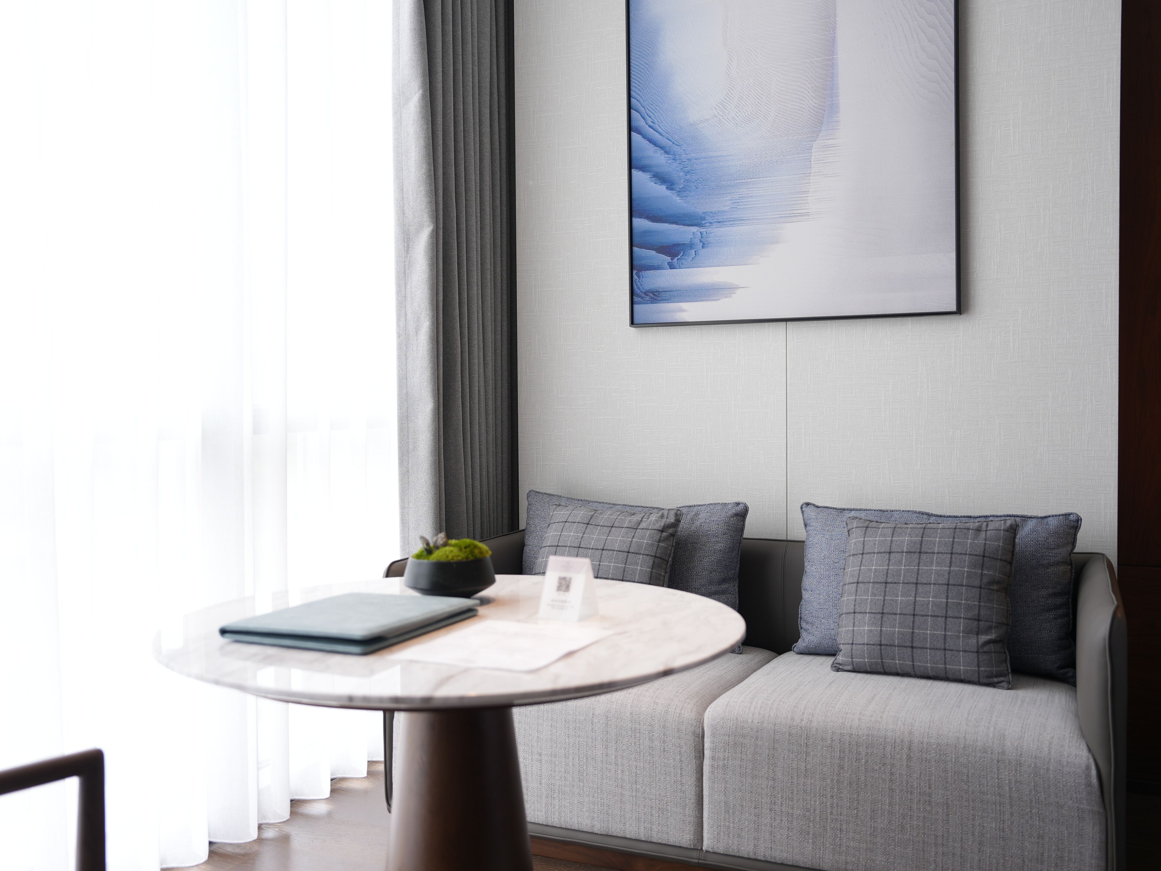Ein modernes Zimmer mit einem runden Tisch, einem grauen Sofa und einem großen, abstrakten Gemälde an der Wand.