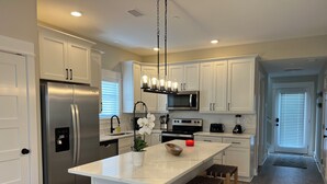 A modern kitchen with white cabinets, stainless steel appliances, and a central island with stools. - EXCEPTIONAL LOCATION - LUXURY VILLA STEPS AWAY FROM THE BEACH AND POOL (Corolla)
