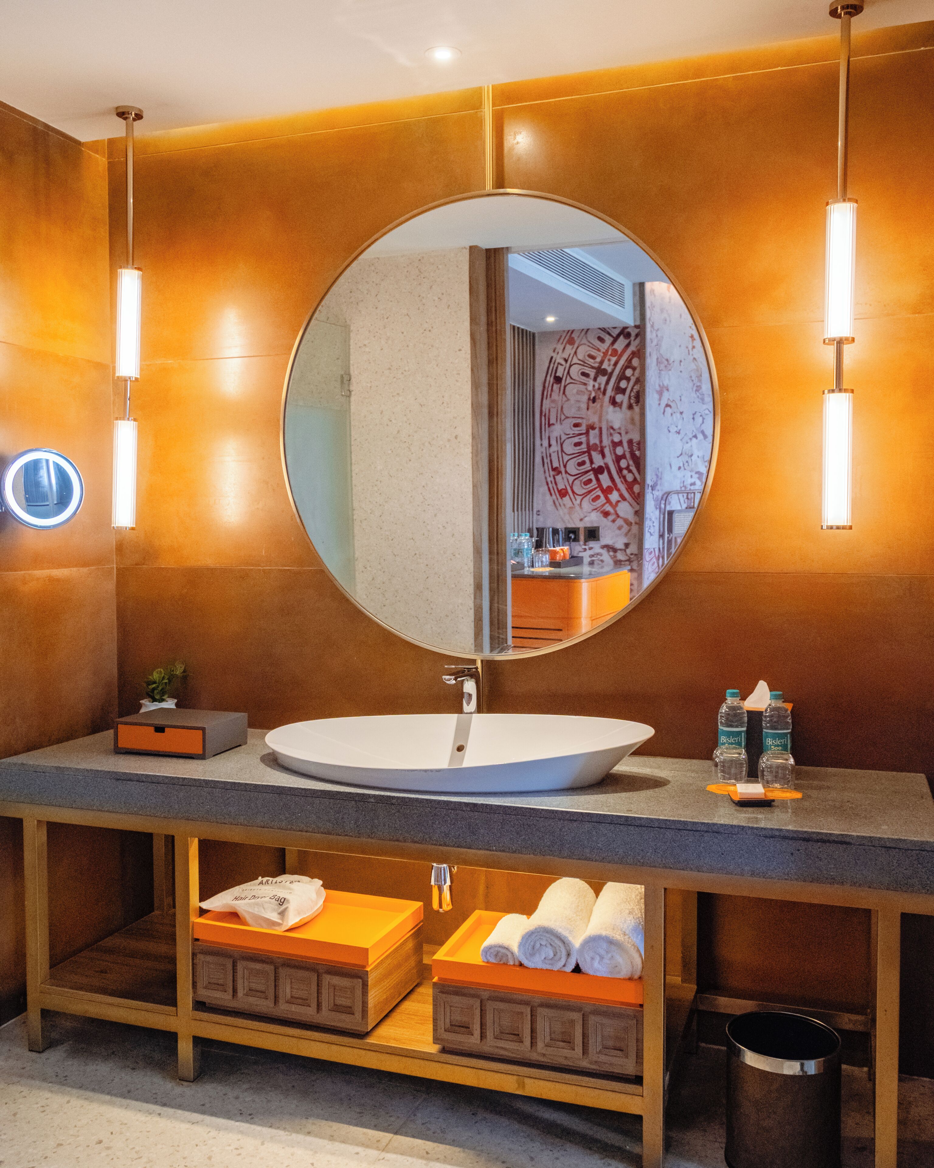 A modern bathroom with a round mirror, a white sink, and two towel dispensers.