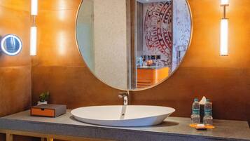 A modern bathroom with a round mirror, a white sink, and two towel dispensers.