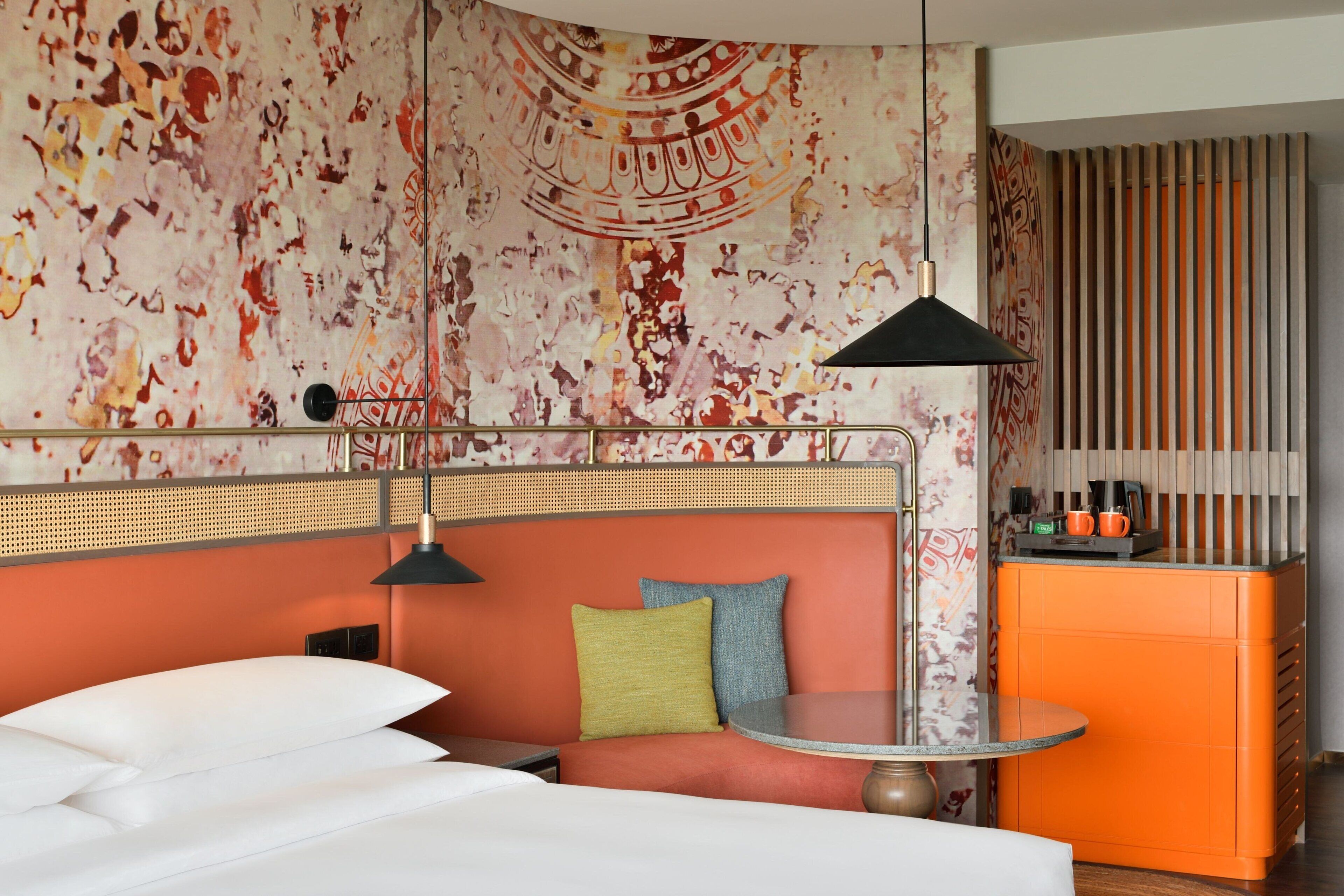 Ein Hotelzimmer mit Bett, rundem Tisch, einer Couch mit Kissen, einer Wand mit Musterdesign und einer Küchenzeile.