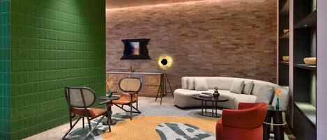 A modern living room with a green wall, a brick wall, a sofa, a red chair, a coffee table, and a TV mounted on the brick wall.