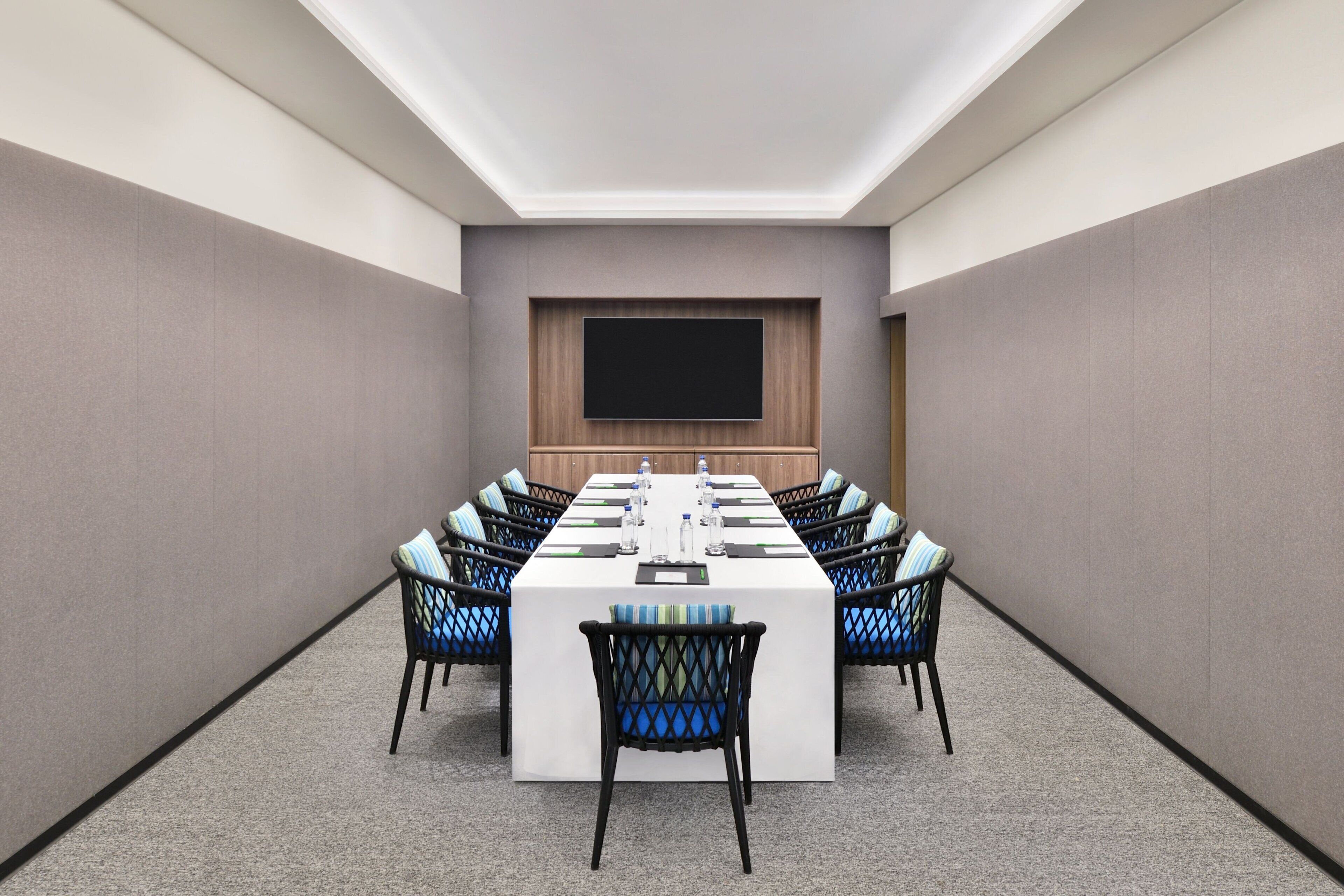 Un salón de conferencias con una larga mesa, sillas, un televisor de pantalla plana y un panel de madera en la pared.