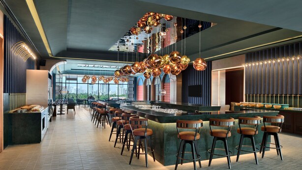 Een moderne bar met een lange toonbank, meerdere krukken en een bijzondere hanglamp.