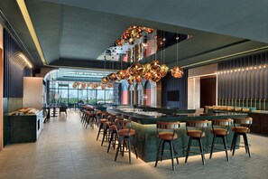 Un espace bar moderne doté d’un long comptoir, de nombreux tabourets et d’un luminaire au plafond au design original.